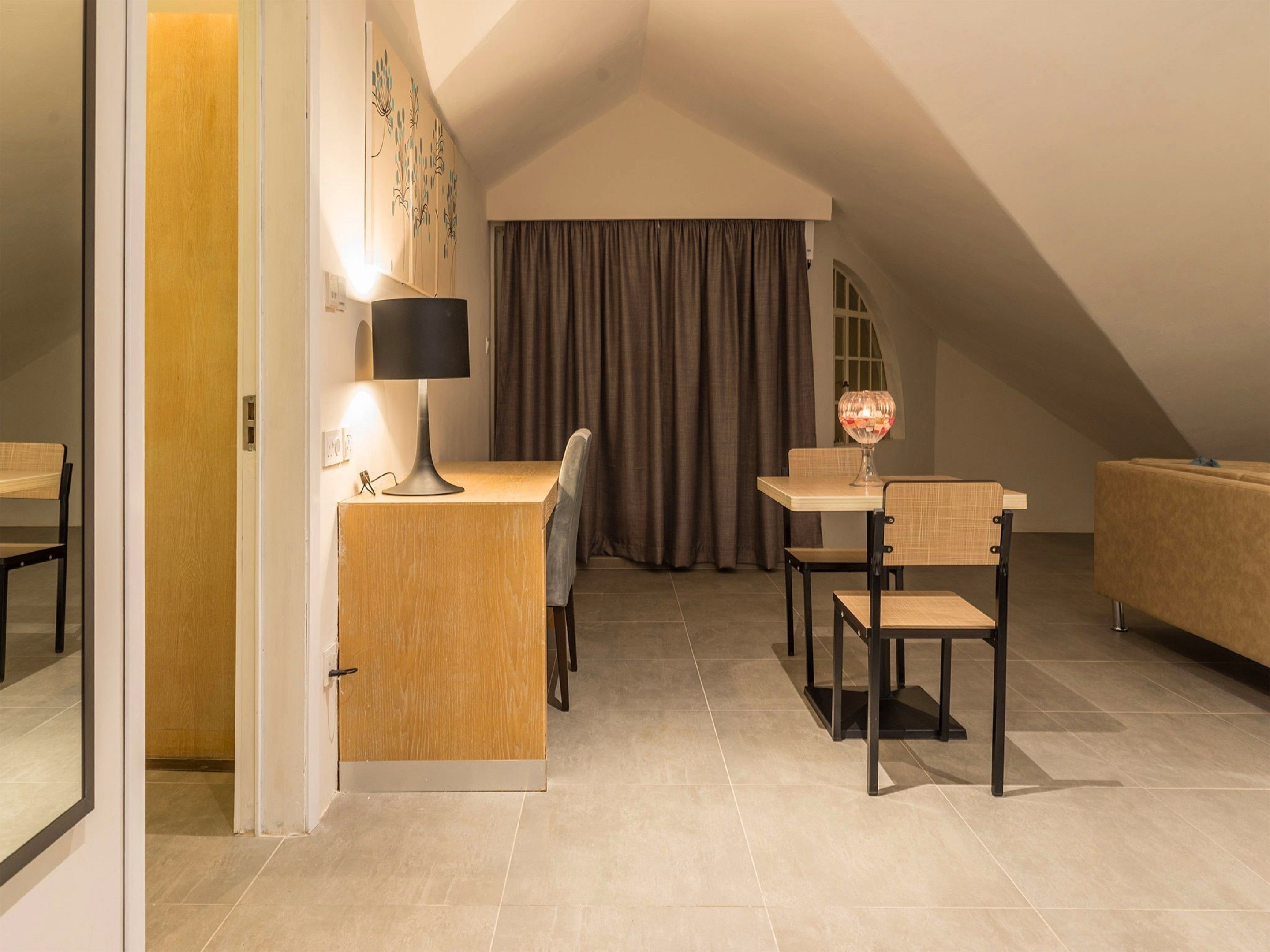 Une pièce confortable et moderne, dotée d’un bureau, de deux chaises, d’une lampe et d’un objet décoratif en verre posé sur une table.