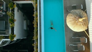 An aerial view of a swimming pool with a person swimming, surrounded by lounge chairs and a large umbrella.