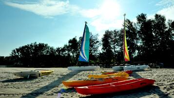 A beach with several kayaks and a sailboat lined up on the sand.