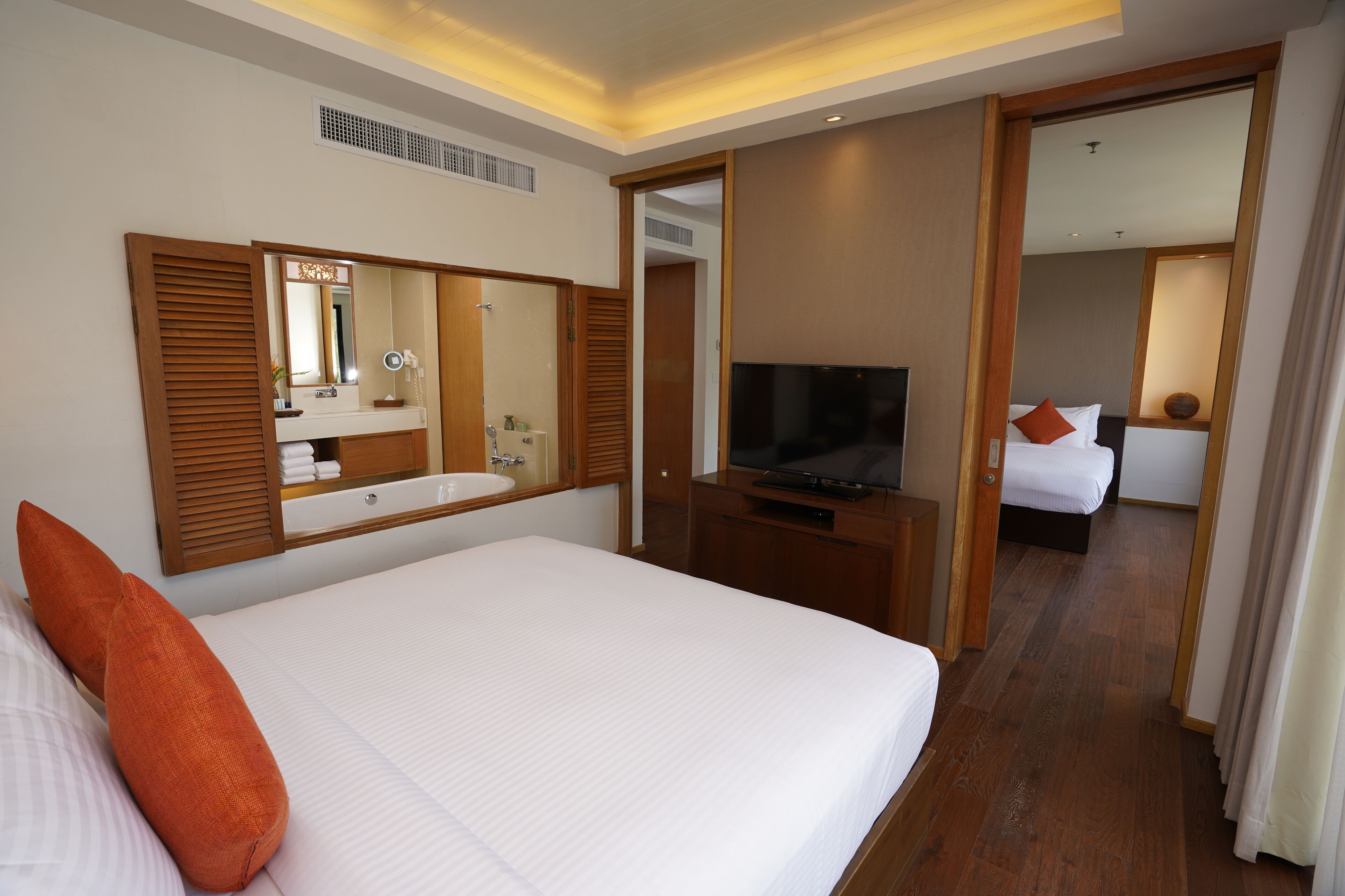 A hotel room with a large bed, a TV, a mirror, and a bathroom visible through an open door.