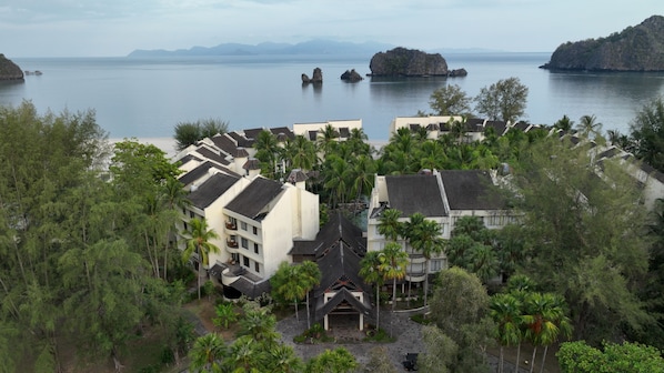 A coastal resort with multiple buildings surrounded by lush greenery and palm trees.