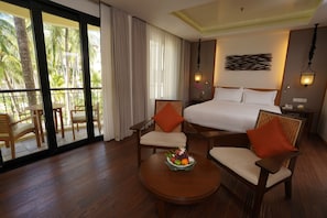 A hotel room with a large bed, two armchairs, a small table with fruit, and a balcony with outdoor furniture.