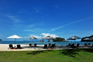 A beach with lounge chairs and umbrellas, a clear sky, and a calm sea.