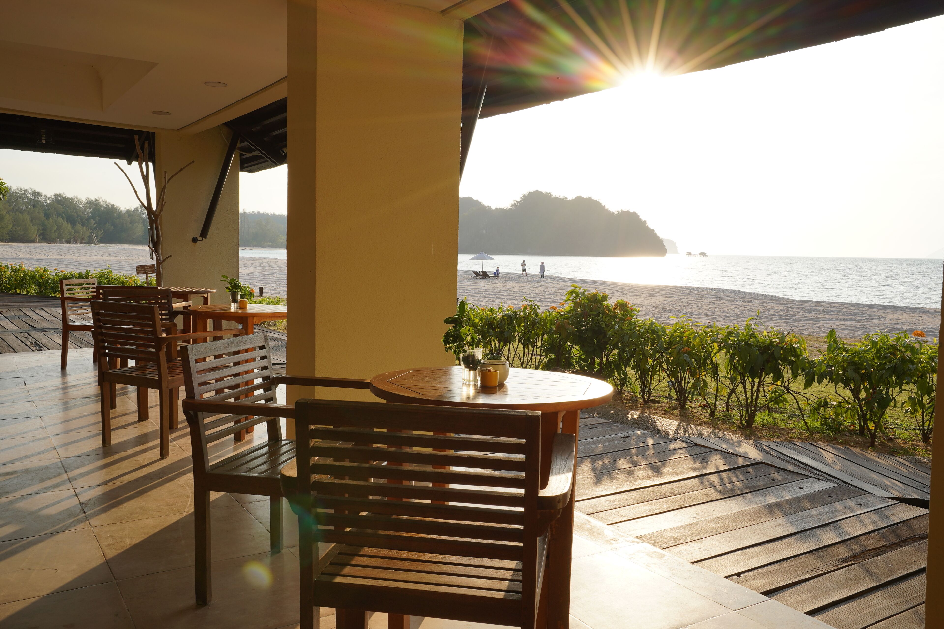 A wooden deck with a round table and chairs, overlooking a body of water with a distant island.