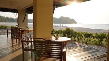 A wooden deck with a round table and chairs, overlooking a body of water with a distant island.