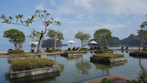 A serene pool area with lounge chairs and umbrellas, surrounded by lush greenery and overlooking a calm body of water. - Tanjung Rhu Resort (Langkawi)
