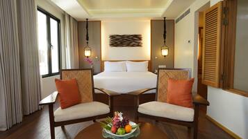 Habitación de hotel con una cama, dos sillas, una mesa con fruta y una ventana con cortinas.