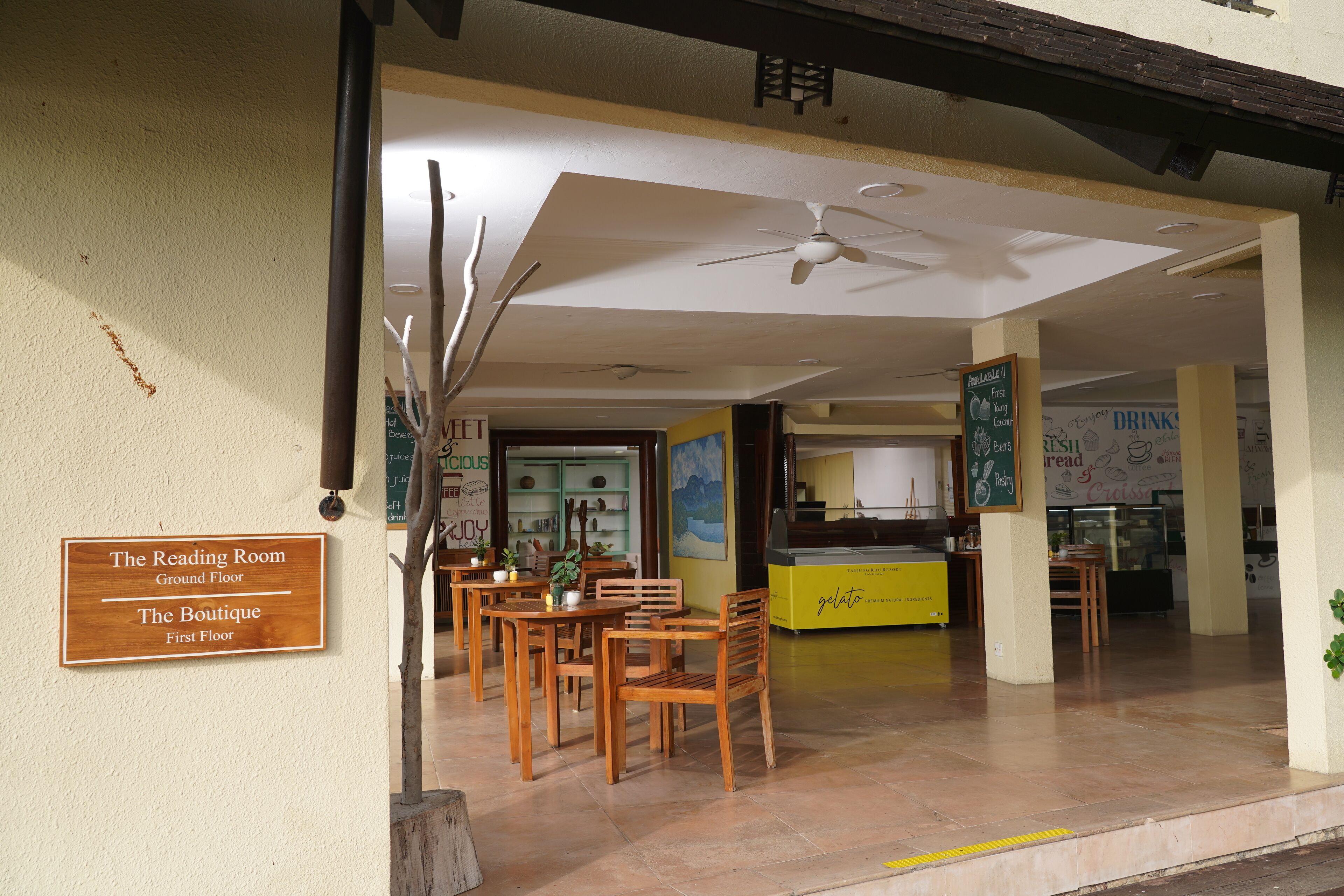 A restaurant with wooden tables and chairs, a ceiling fan, and a sign indicating 'The Reading Room' and 'The Boutique'.