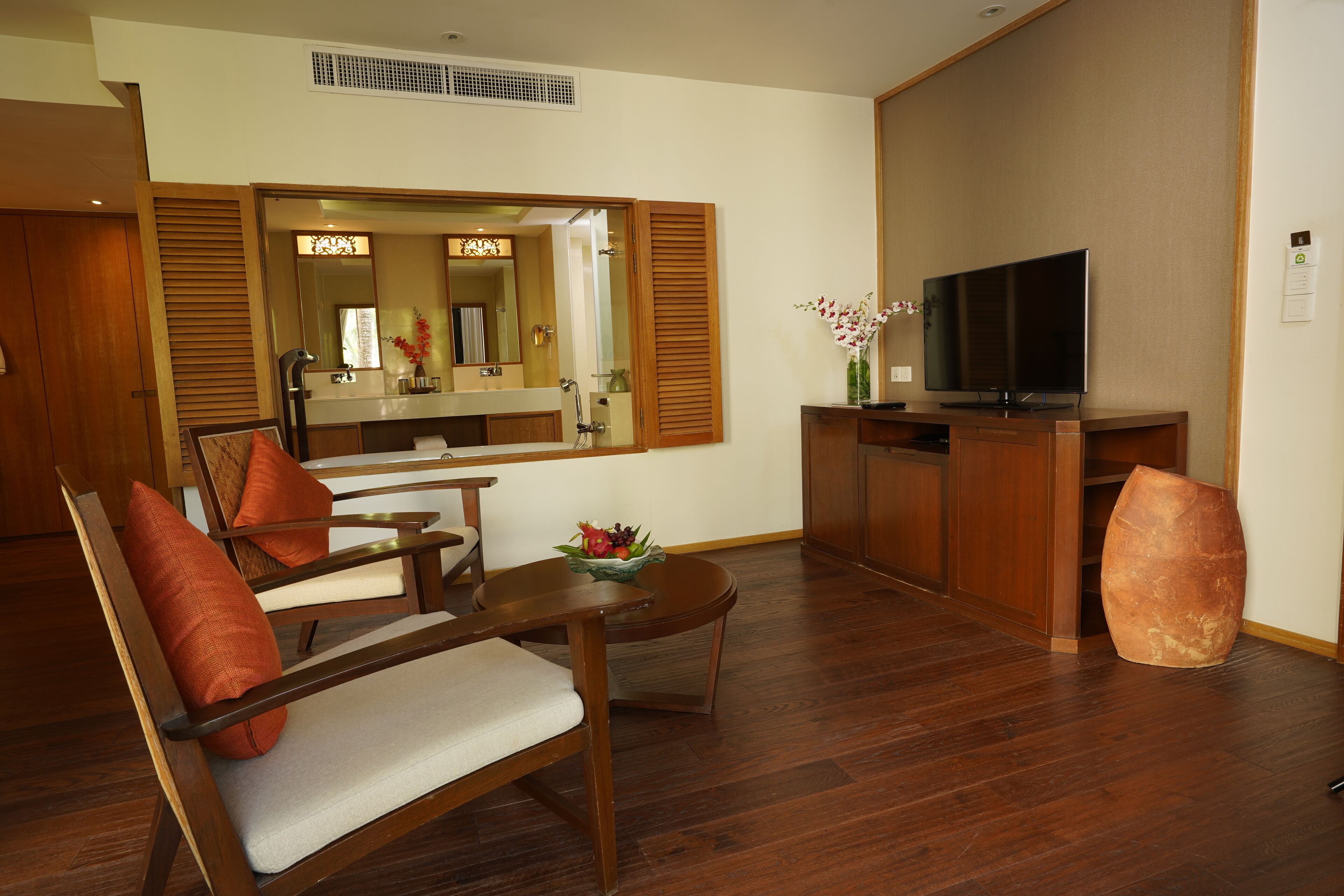A hotel room with a wooden floor, a television, a wooden desk, a chair, and a large mirror.
