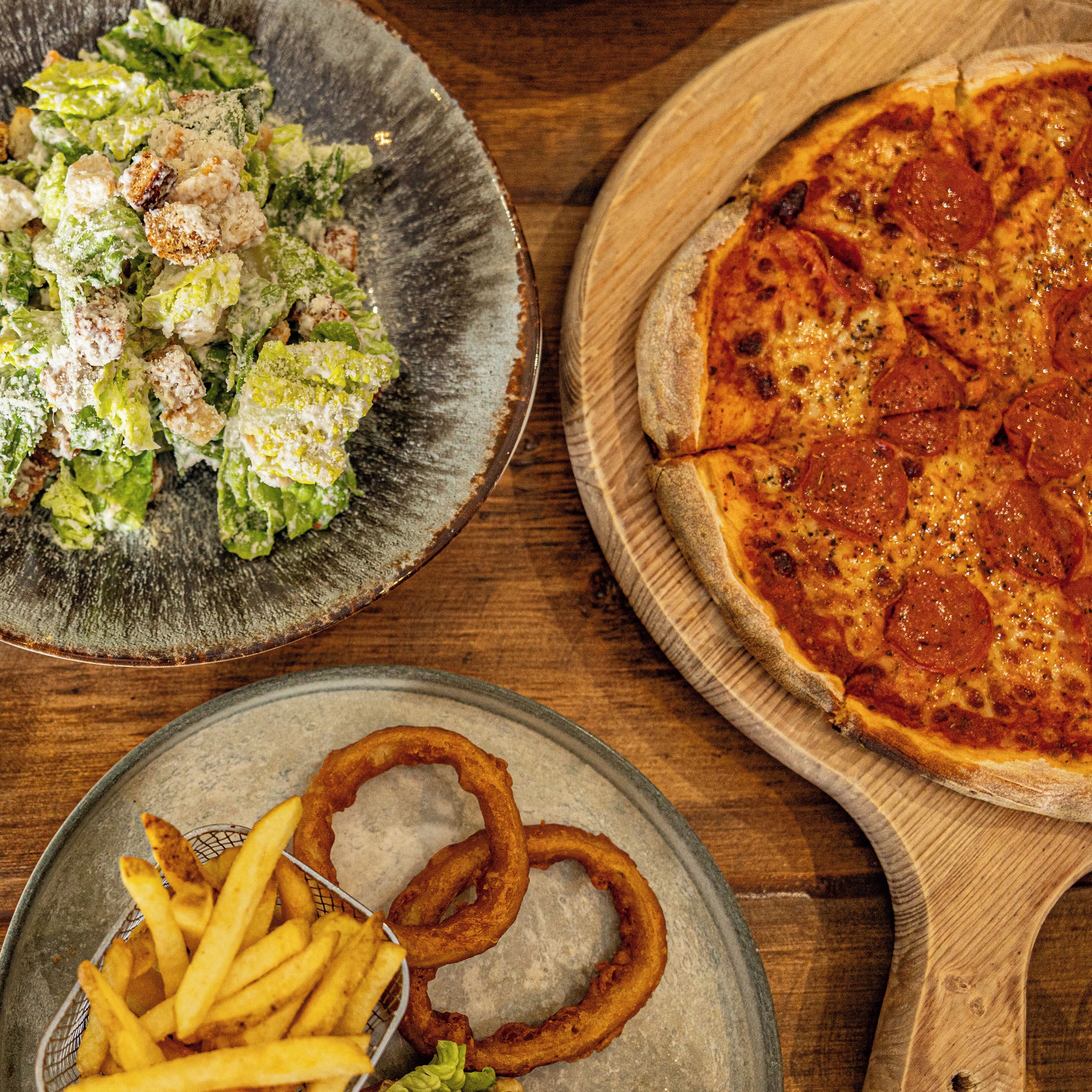 A wooden table with a pizza, a salad, and French fries.