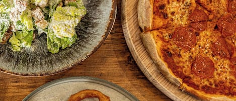 A wooden table with a pizza, a salad, and French fries.