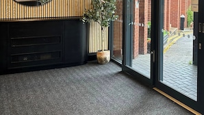 A modern interior with a wooden panel wall, a round mirror, a potted plant, and a glass door leading outside.