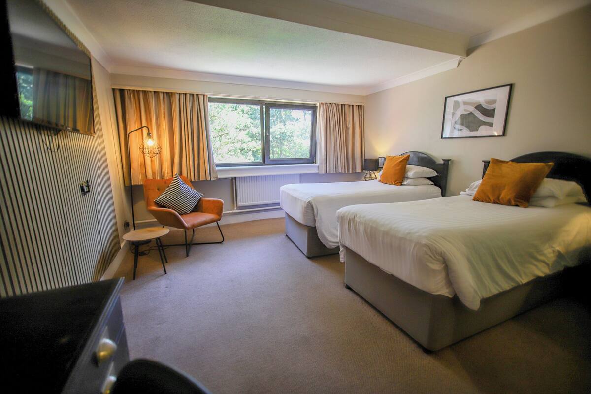 A hotel room with two beds, a chair, a desk, and a window with curtains.