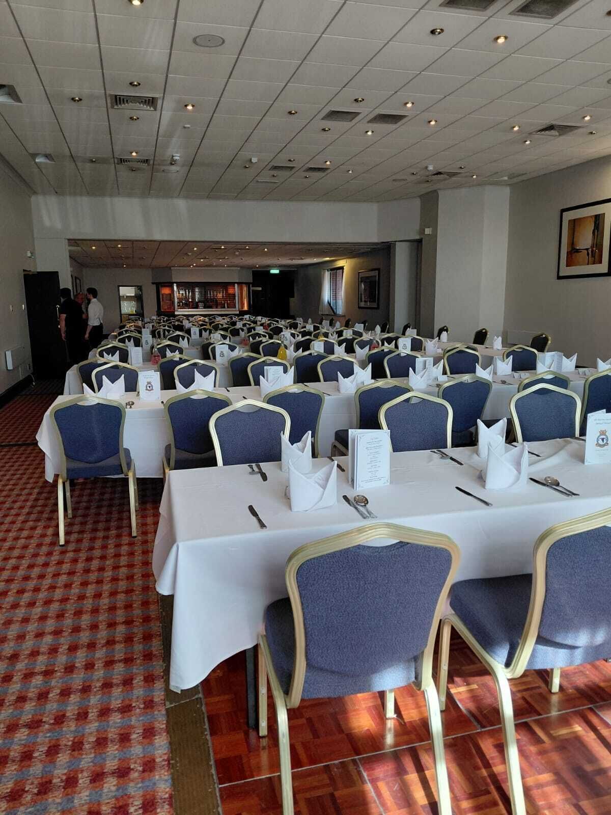 Une salle de conférence avec des rangées de tables et de chaises, une moquette à motifs et un plafond doté d’un éclairage encastré.