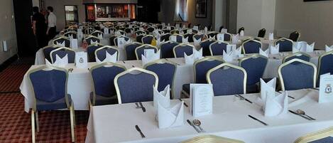 A conference room with rows of tables and chairs, a patterned carpet, and a ceiling with recessed lighting.