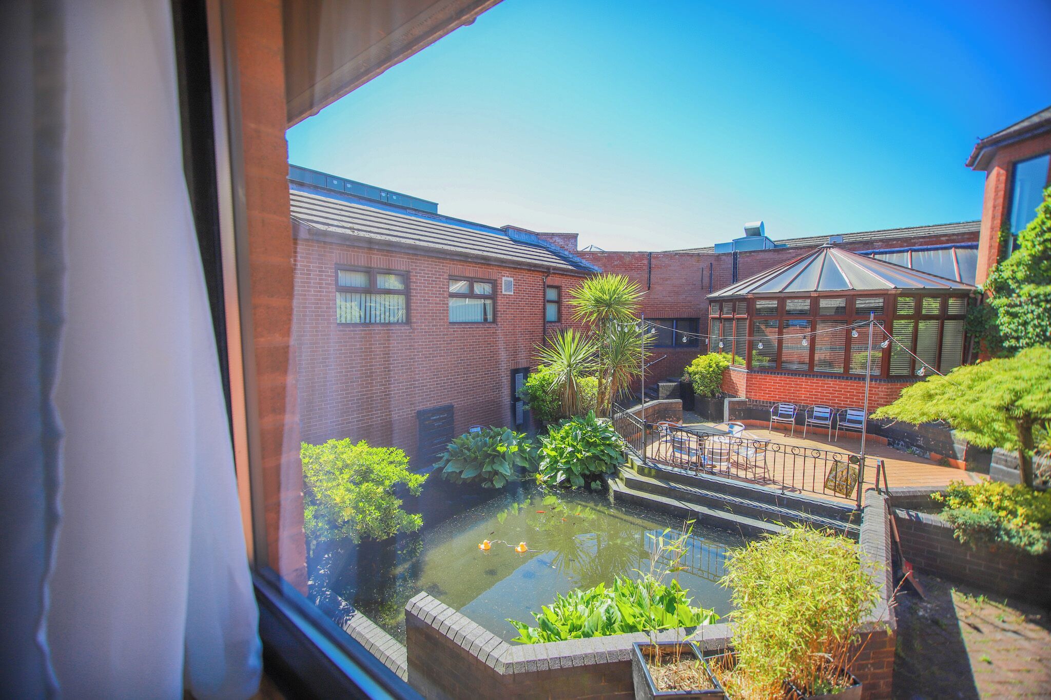 A courtyard with a pond, brick buildings, and a covered seating area.