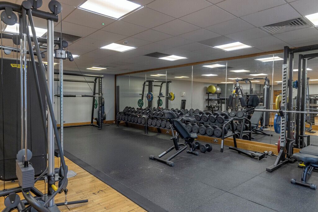 Un gimnasio con equipamiento de levantamiento de pesas, mancuernas y máquinas de ejercicio.