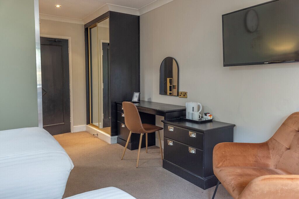 Ein Hotelzimmer mit Bett, Schreibtisch, Stuhl, Fernseher und Spiegel.
