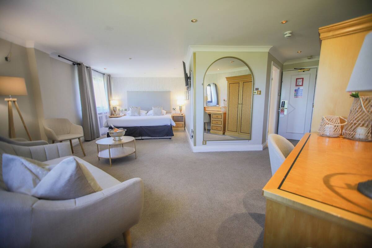 A hotel room with a bed, a desk, a chair, a sofa, and a mirror.