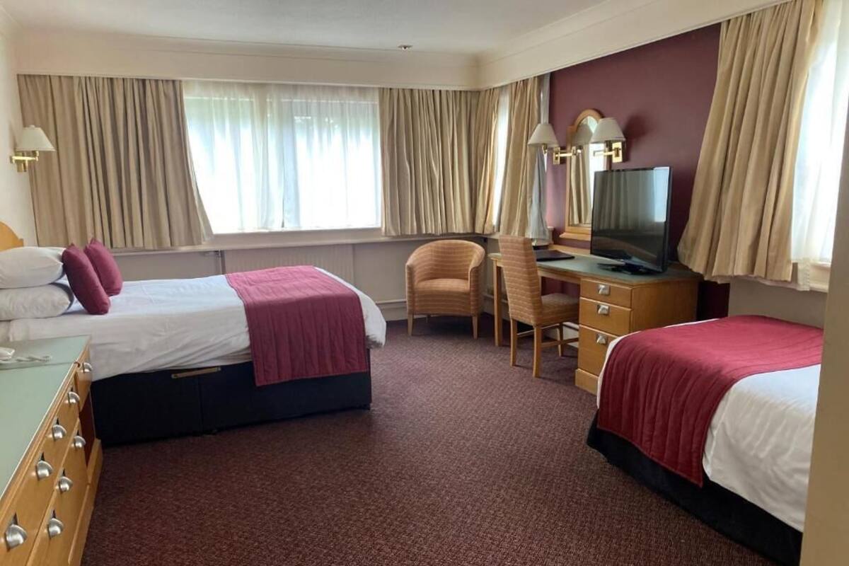 A hotel room with two beds, a desk, a television, and a chair.