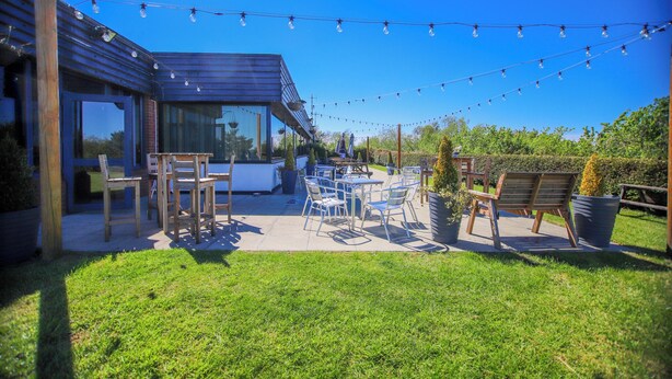 An outdoor patio with a dining table and chairs, string lights, and a modern building structure.