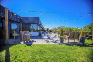 An outdoor patio with a dining table and chairs, string lights, and a modern building structure. - Forest Hills Hotel & Country Club (Frodsham)