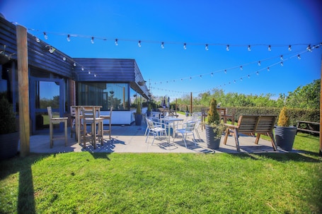 An outdoor patio with a dining table and chairs, string lights, and a modern building structure.. Forest Hills Hotel & Country Club