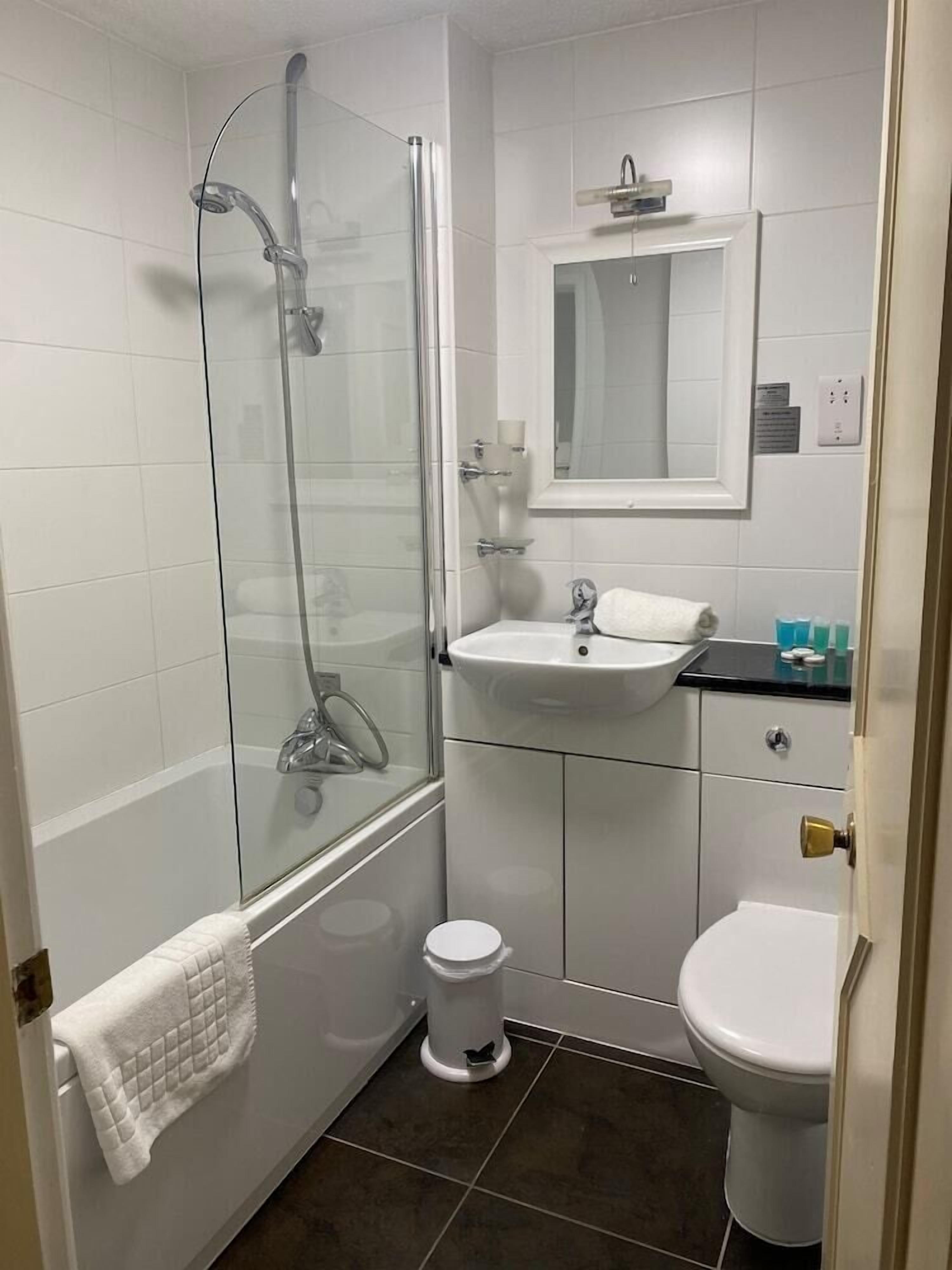 Ein Badezimmer mit einer Duschkabine, einem weißen Waschbecken, einer Toilette und einem Spiegel über dem Waschbecken.