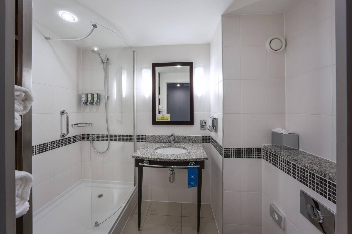 Un baño moderno con cabina de ducha de vidrio, un lavamanos con espejo encima y suelo de baldosas.