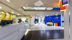 Een moderne hotelontvangsthal met een receptiebalie, zithoek en een groot muurschilderij.