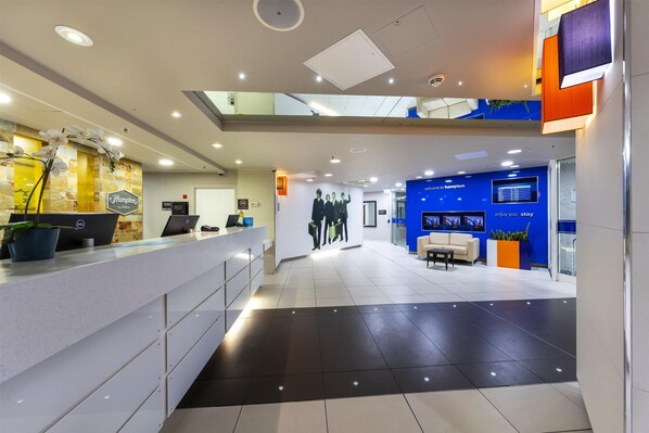 A modern hotel reception area with a reception desk, seating area, and a large wall mural.