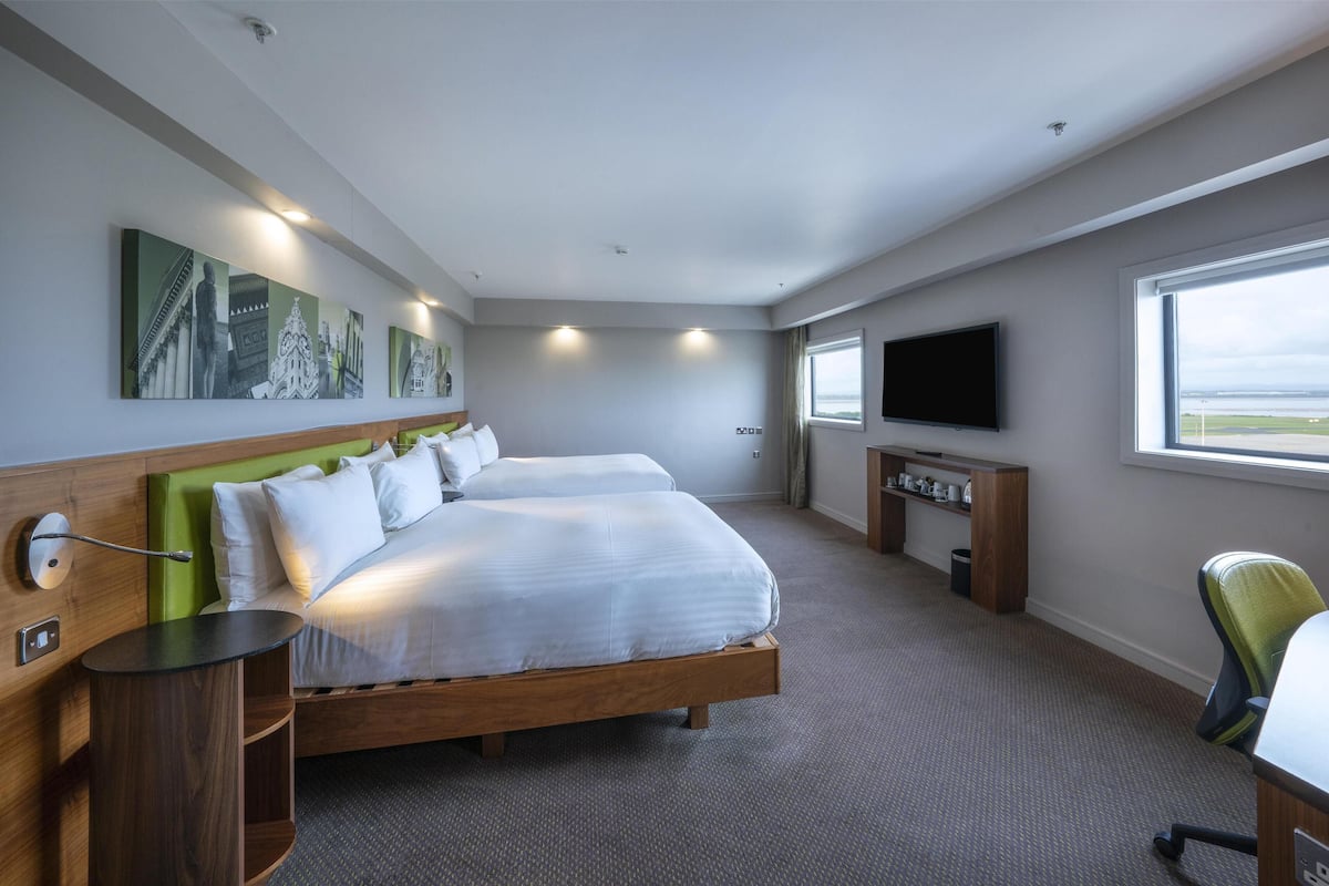 Habitación de hotel con una cama grande, televisor, escritorio y cuadros en la pared.