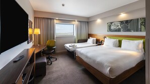 Een hotelkamer met een groot bed, een bureau met stoel, een televisie en een raam met gordijnen.