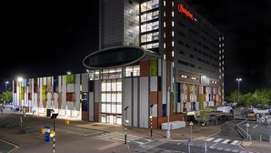 A multi-story hotel with a prominent "Hampton" sign, large windows, and a modern facade with vertical panels.