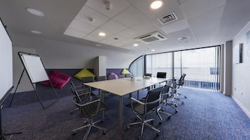 Un salón de conferencias con una gran mesa, sillas, una pizarra y almohadones de colores.
