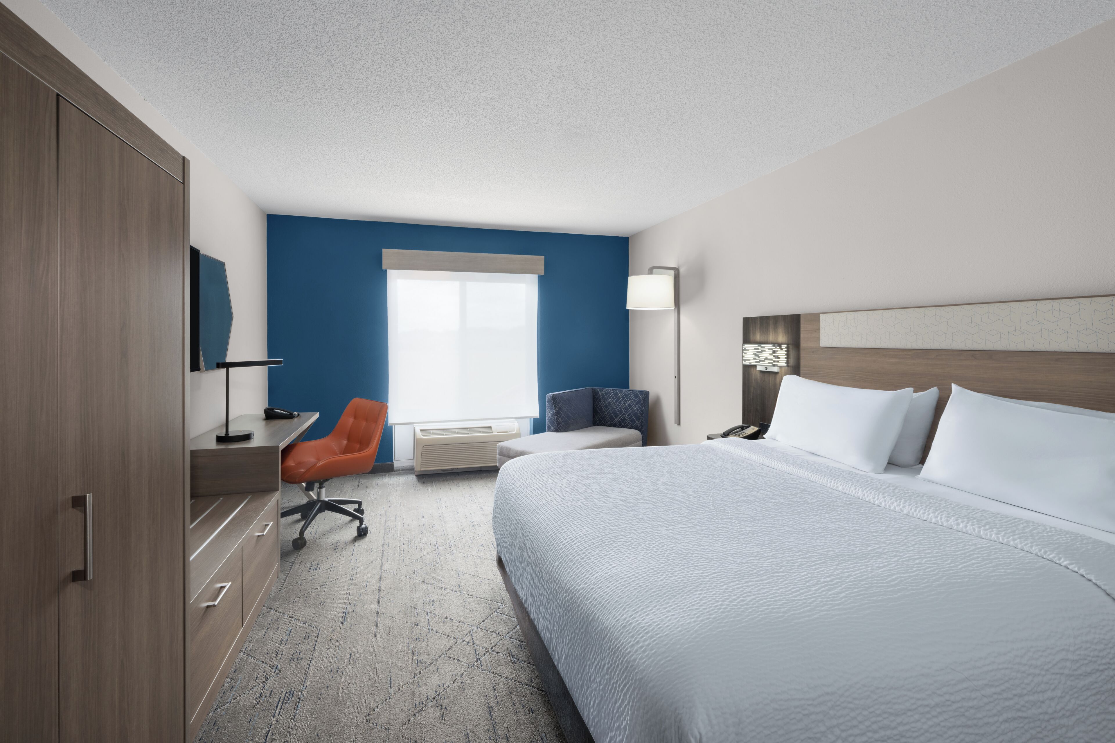 A hotel room with a large bed, a desk with a chair, a TV, and a window with blinds.