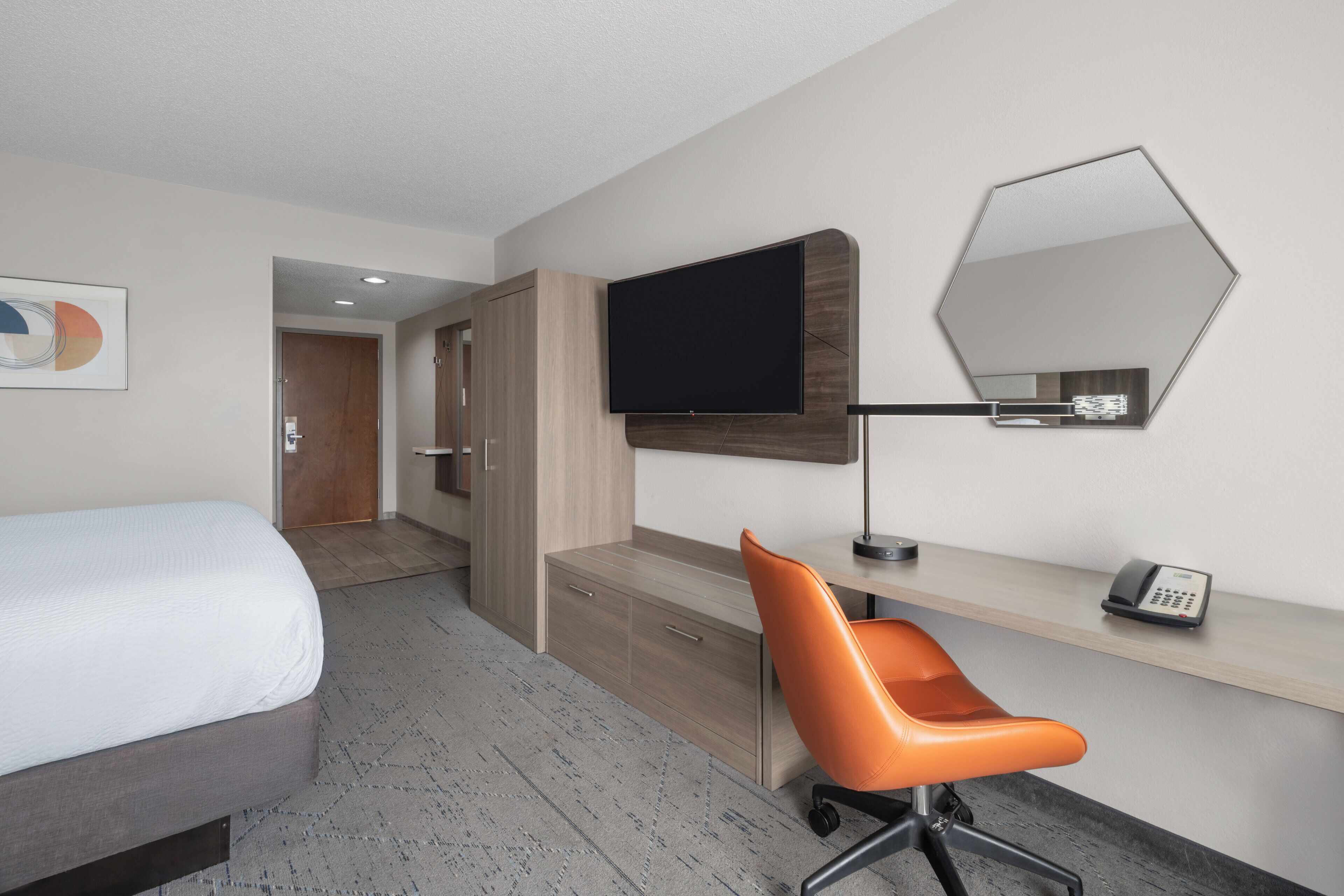 Une chambre d’hôtel comprenant un lit, un bureau avec une chaise, un téléviseur à écran plat, un téléphone et un miroir au mur.