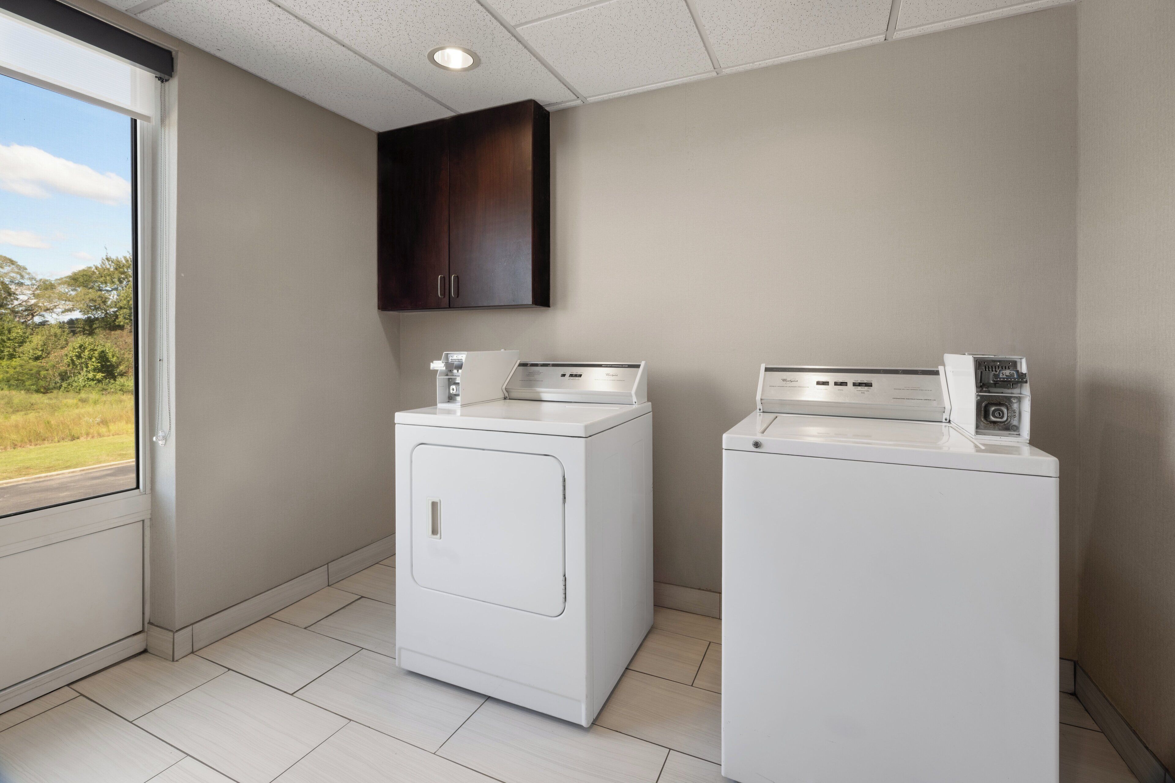 A laundry room with two white front-loading washers and a dark wooden cabinet above them.