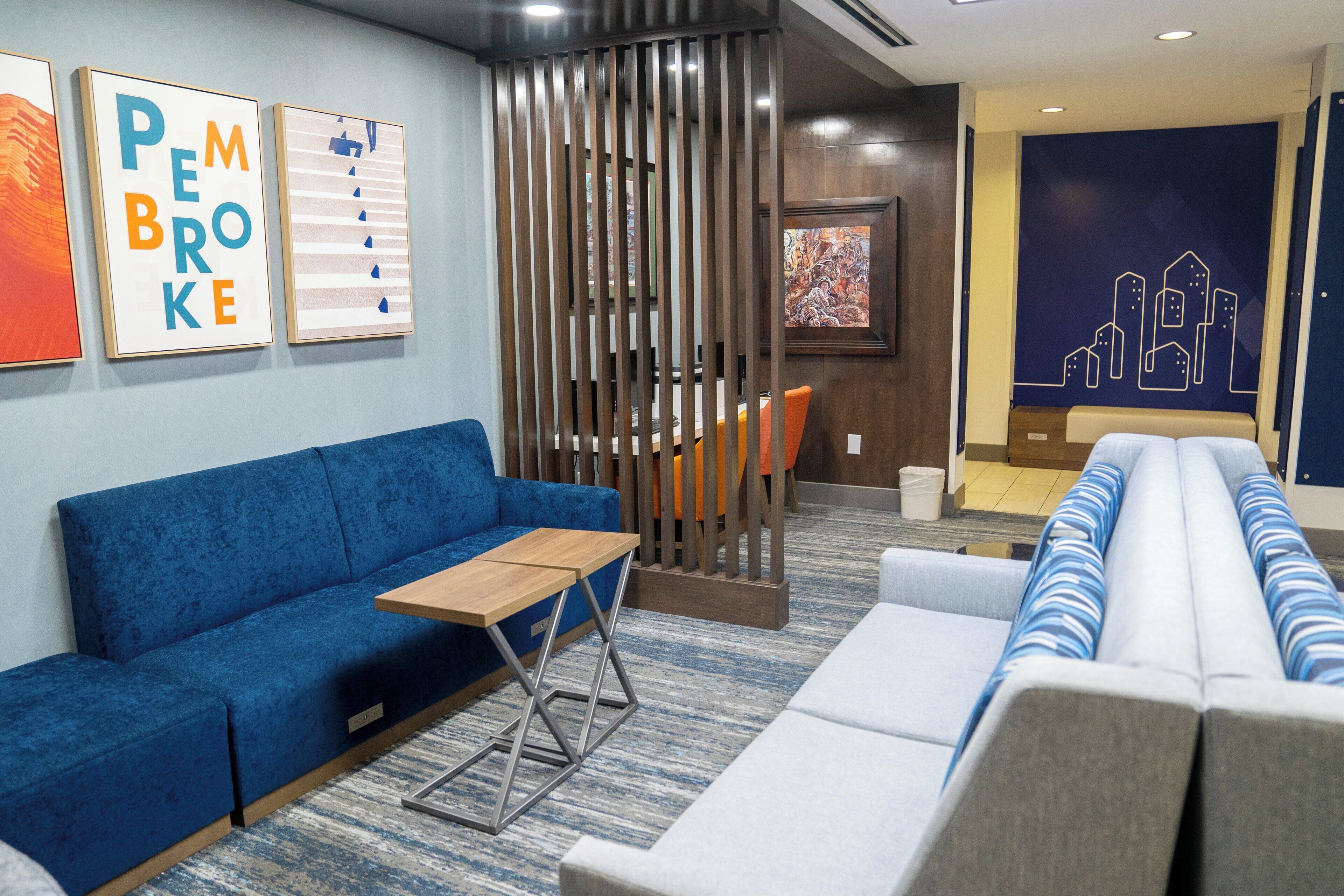 A modern hotel lobby with a blue sofa, a wooden table, and a cityscape mural.
