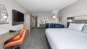 Een hotelkamer met een bed, een bureau met stoel, een televisie, een bureaulamp en een kleine kitchenette.