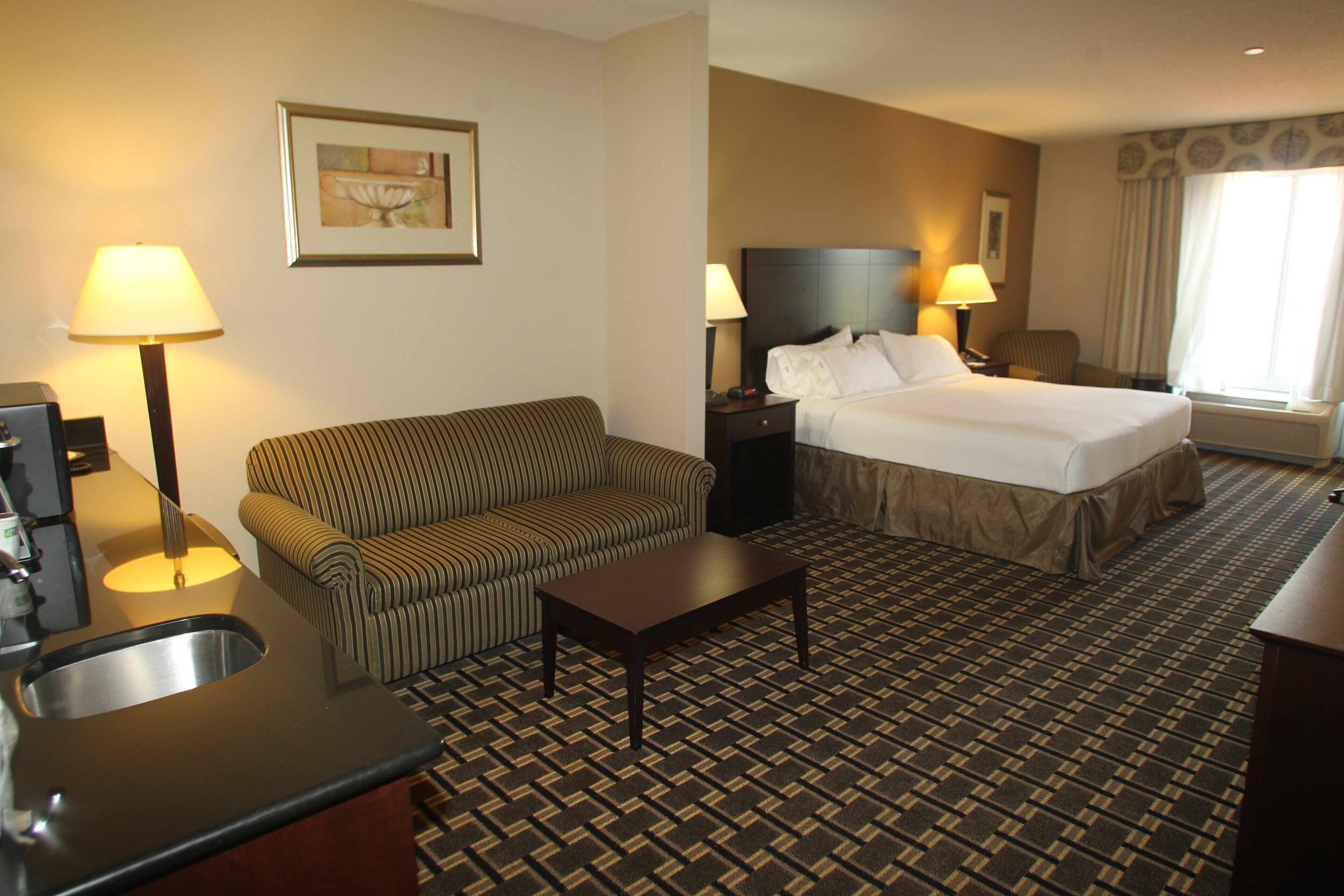 A hotel room with a bed, a sofa, a desk, a lamp, and a painting on the wall.