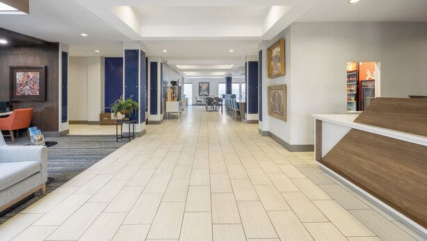 Een ruime hotellobby met een lange receptiebalie, een zithoek en een goed zicht op de eetruimte op de achtergrond.
