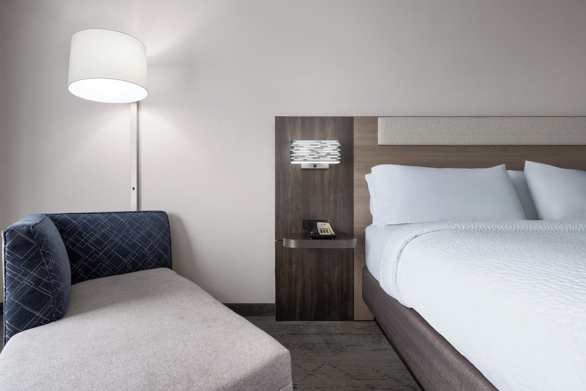 Ett hotellrum med en säng, ett sängbord med en lampa och ett litet sidobord.