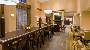 A hotel lobby with a long reception desk, multiple seating areas, a television, and a fireplace. - Hampton Inn & Suites Peoria at Grand Prairie, IL (Peoria)