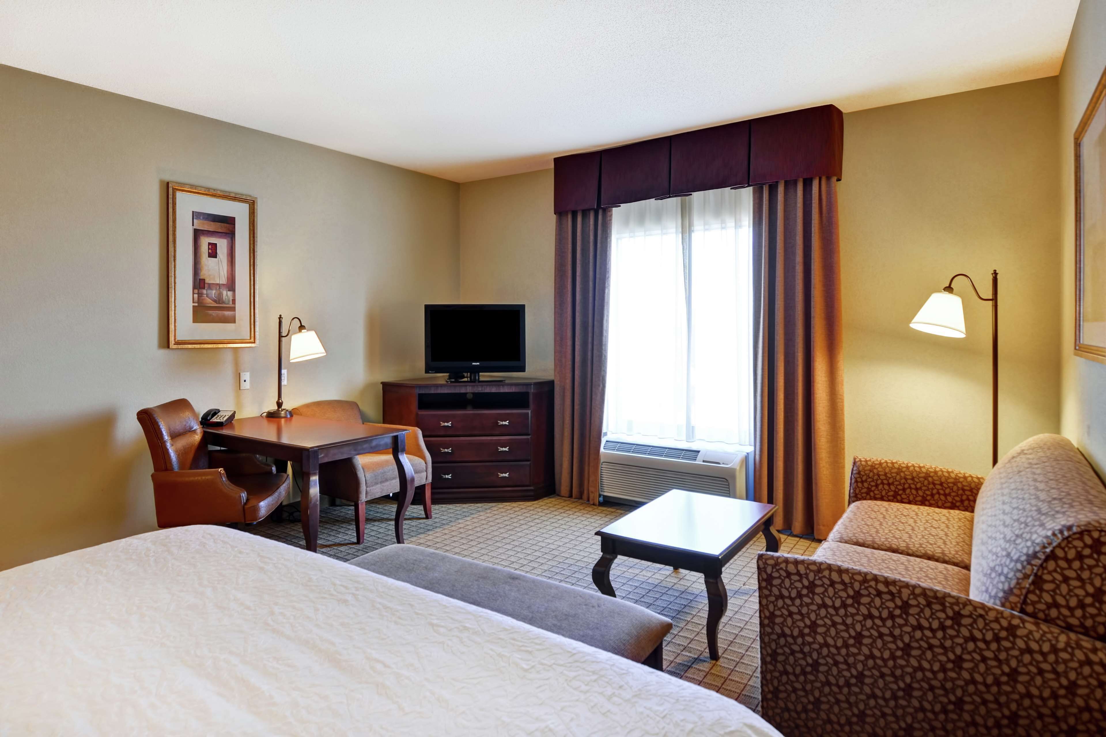 A hotel room with a large bed, a desk with a chair, a television, and a sofa.