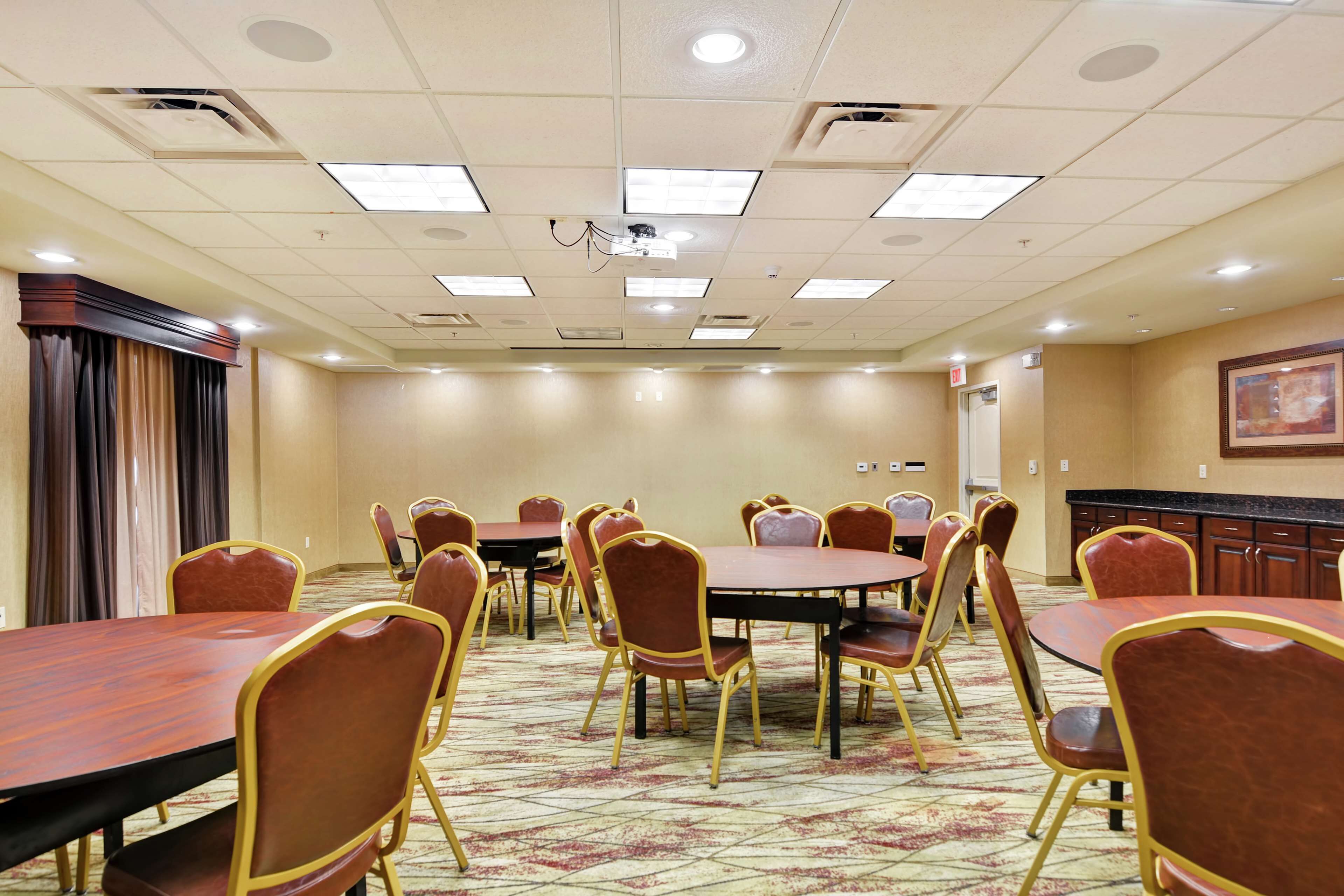 A conference room with multiple tables and chairs, a carpeted floor, and a ceiling with recessed lighting.