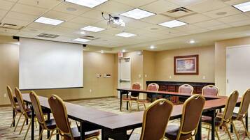 A conference room with a long table, multiple chairs, a projector screen, and a carpeted floor.