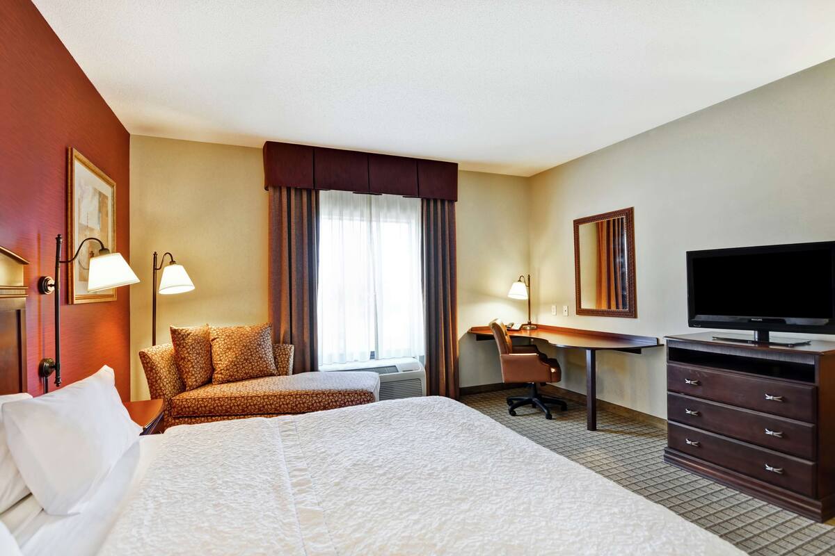 A hotel room with a large bed, a desk with a chair, a television, and a window with curtains.