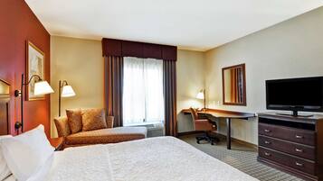 A hotel room with a large bed, a desk with a chair, a television, and a window with curtains.