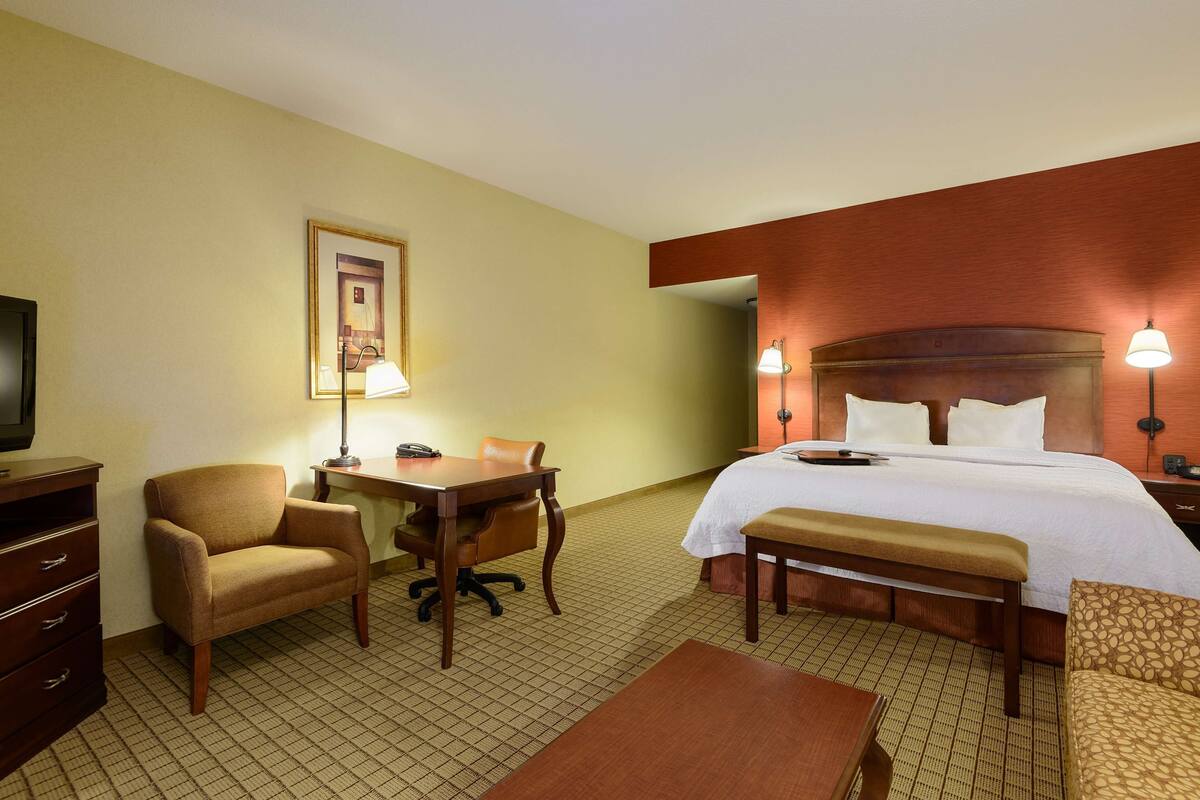 A hotel room with a bed, desk, chair, and a television.